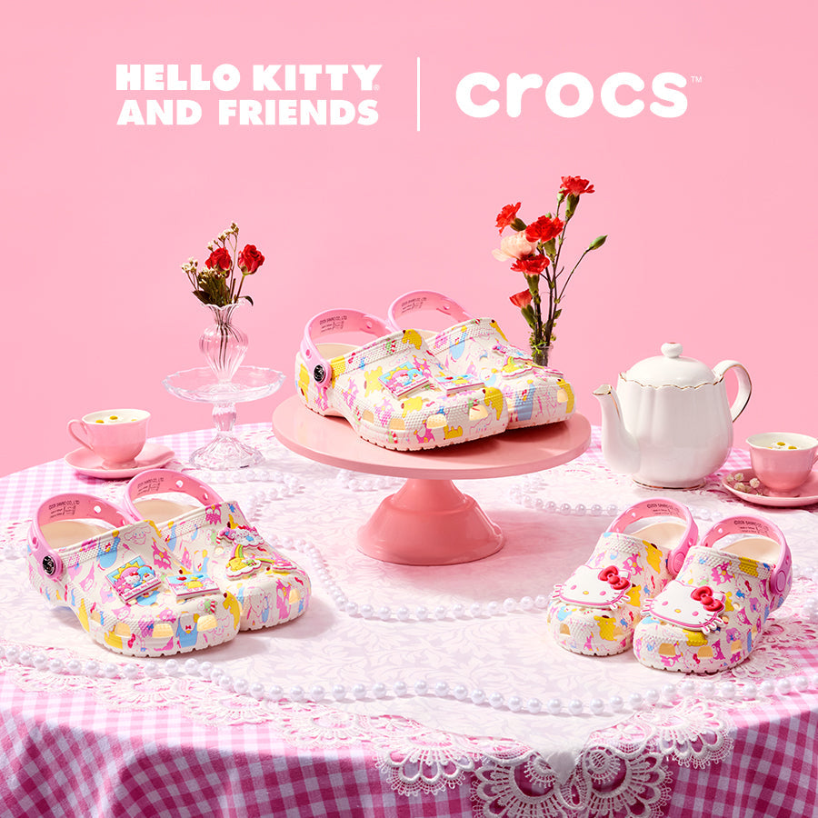 Clogs on a pink table with a tea set and flowers, branded with Crocs and Hello Kitty.