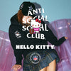 A person wearing a black Anti Social Social Club x Hello Kitty hoodie and matching black cap, seated on a translucent pink inflatable pool float against a light blue background. Large overlaid text reads 'ANTI SOCIAL SOCIAL CLUB', 'HELLO KITTY', and 'OFFICIALLY LICENSED PRODUCT' with NFL logos visible.