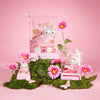 Decorative setup with a Hello Kitty figurine, flowers, and a pink background.