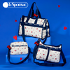 Three LeSportsac tote and shoulder bags in a matching off-white fabric with a red and black heart pattern, navy blue straps and trim, and red bow accents, displayed on blue blocks against a blue background with red heart graphics.