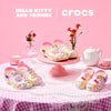 Clogs on a pink table with a tea set and flowers, branded with Crocs and Hello Kitty.