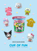 A cup-shaped Hello Kitty and Friends toy box centered on a light blue background, surrounded by small Hello Kitty character figures in pink, white, green, yellow, and black. Text at the bottom reads 'NEW IN BLIND BOXES CUP OF FUN'.
