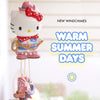 A Hello Kitty wind chime hanging in front of a bright, softly blurred window. The wind chime features a white Hello Kitty character wearing a red bow, red polka-dot scarf, blue top, and pink boots, with a rope wrapped around its neck.