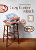 Stack of clothing on a stool with 'Cozy Corner Merch' branding and cartoon character illustrations.